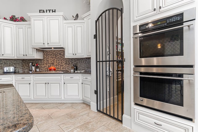 kitchen featuring stainless steel appliances, dark stone countertops, white cabinets, and backsplash