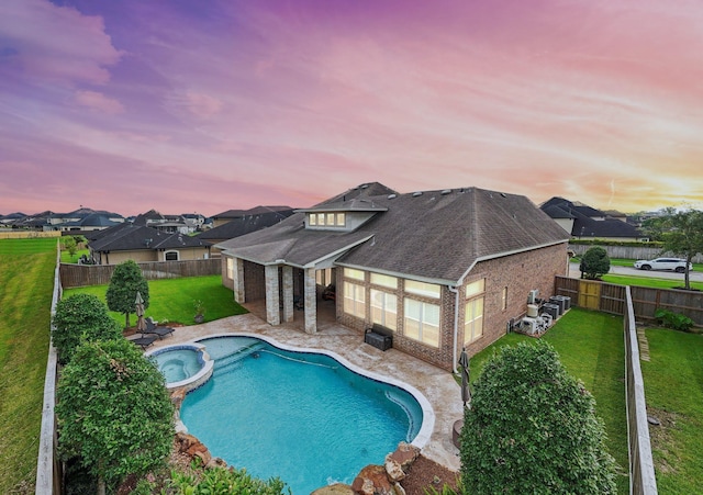 pool at dusk with an in ground hot tub and a yard