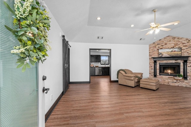 interior space with lofted ceiling, a barn door, a stone fireplace, ceiling fan, and dark hardwood / wood-style floors