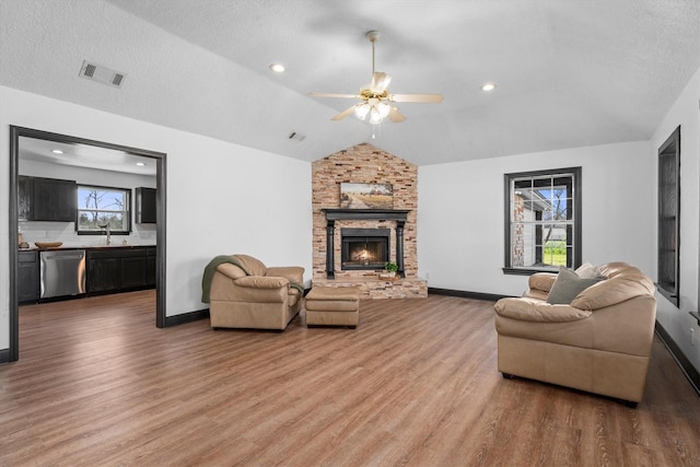 living room featuring hardwood / wood-style flooring, vaulted ceiling, a textured ceiling, and a stone fireplace