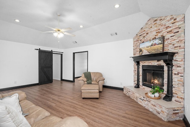 living room with a stone fireplace, lofted ceiling, ceiling fan, hardwood / wood-style floors, and a barn door