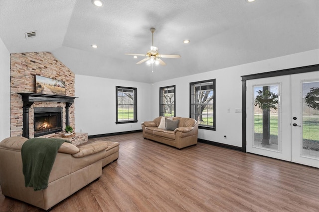 living room with lofted ceiling, wood-type flooring, a stone fireplace, a textured ceiling, and ceiling fan