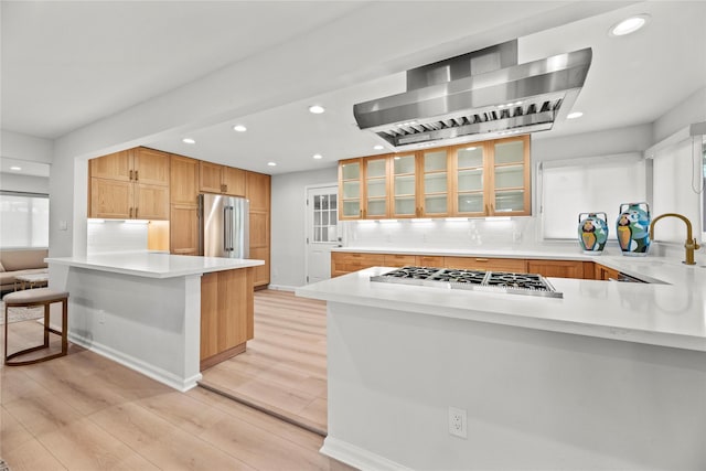 kitchen featuring sink, appliances with stainless steel finishes, light hardwood / wood-style floors, kitchen peninsula, and exhaust hood