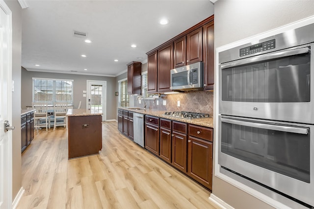 kitchen with sink, light stone counters, a center island, stainless steel appliances, and tasteful backsplash