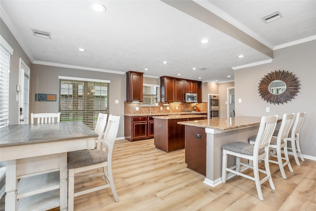 kitchen with stainless steel appliances, a center island, light hardwood / wood-style flooring, light stone countertops, and decorative backsplash