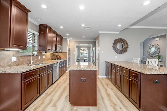 kitchen with appliances with stainless steel finishes, light wood-type flooring, backsplash, a center island, and sink