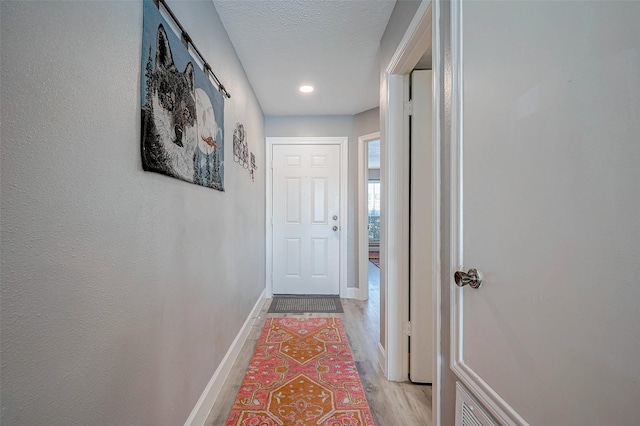 hall with a textured ceiling, light wood finished floors, and baseboards