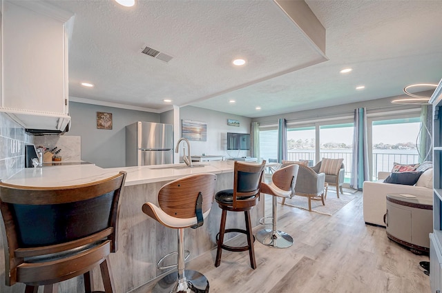 kitchen with a breakfast bar area, a peninsula, light wood-style floors, light countertops, and freestanding refrigerator