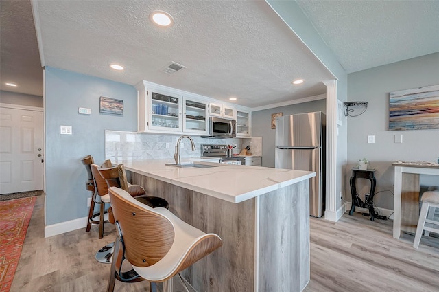 kitchen with a peninsula, a breakfast bar, light countertops, appliances with stainless steel finishes, and glass insert cabinets