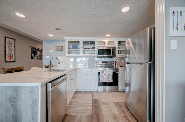 kitchen with white cabinets, light stone counters, glass insert cabinets, stainless steel appliances, and a sink