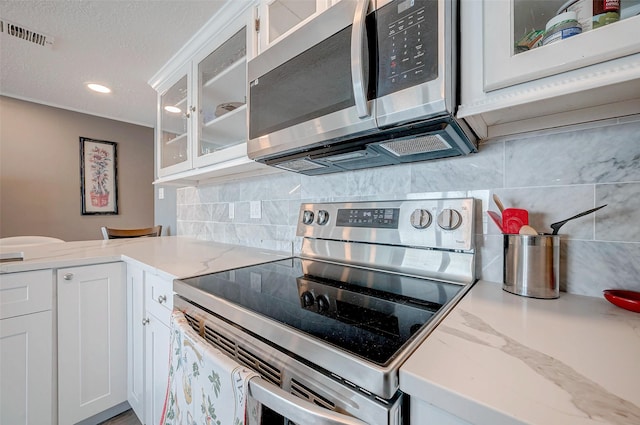 kitchen featuring tasteful backsplash, white cabinets, glass insert cabinets, appliances with stainless steel finishes, and a textured ceiling