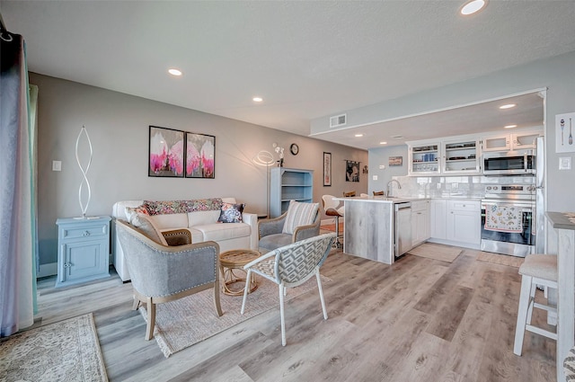 living room featuring light wood-type flooring, visible vents, a textured ceiling, and recessed lighting