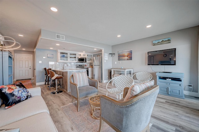 living area featuring baseboards, light wood finished floors, visible vents, and recessed lighting