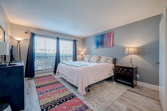 bedroom with a textured ceiling, baseboards, and wood finished floors