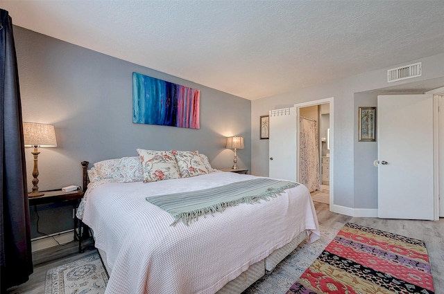 bedroom with a textured ceiling, baseboards, visible vents, and light wood-style floors