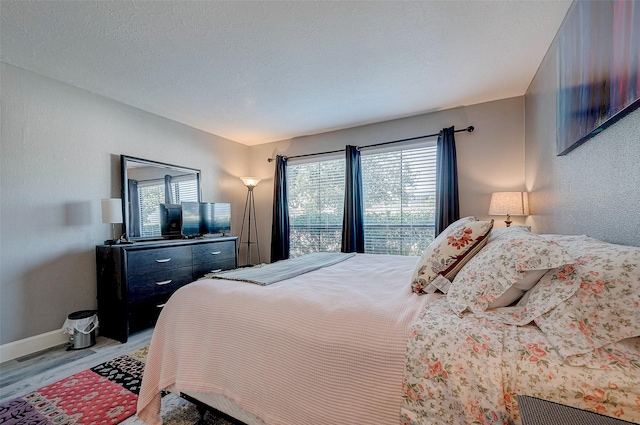 bedroom with a textured ceiling, a textured wall, light wood-style flooring, and baseboards