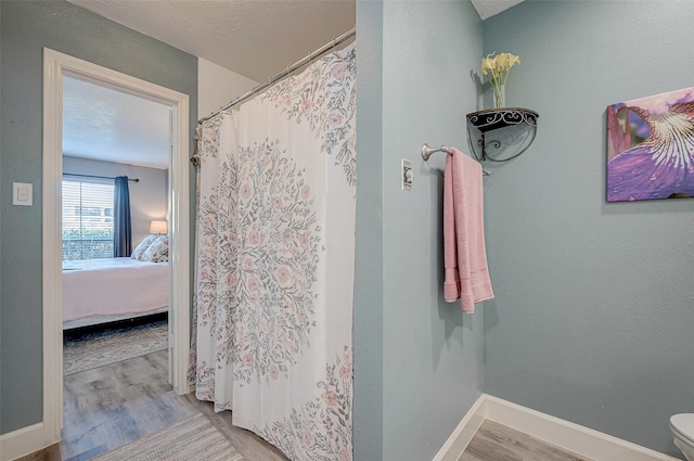 bathroom with baseboards, toilet, ensuite bath, wood finished floors, and a textured ceiling