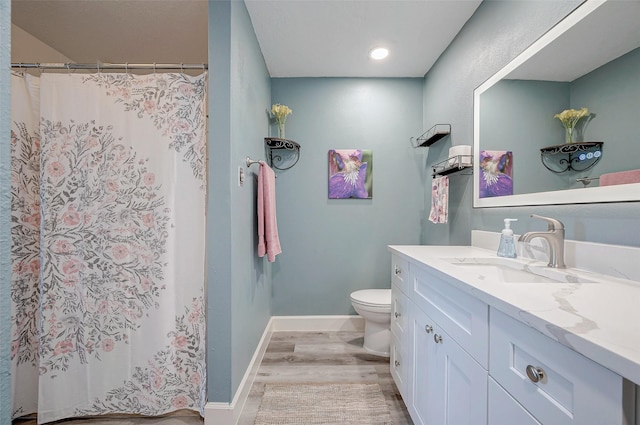 bathroom featuring toilet, baseboards, wood finished floors, and vanity