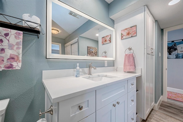 bathroom with a textured wall, wood finished floors, vanity, and visible vents