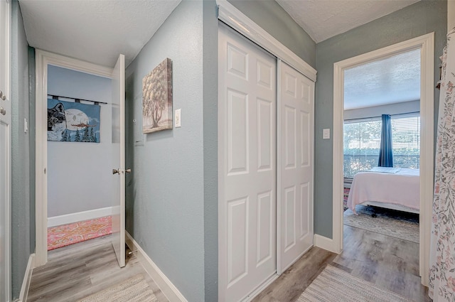 corridor featuring a textured ceiling, baseboards, and light wood-style floors