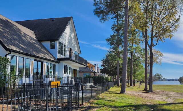 view of home's exterior featuring a water view, roof with shingles, fence, and stucco siding