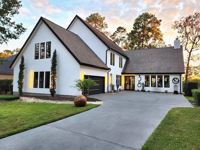 view of front of house with driveway, a shingled roof, a chimney, an attached garage, and a front lawn