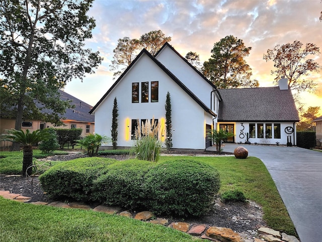 view of front of property with driveway, a shingled roof, a chimney, a yard, and stucco siding