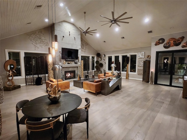 living room with a large fireplace, visible vents, a ceiling fan, light wood-type flooring, and high vaulted ceiling