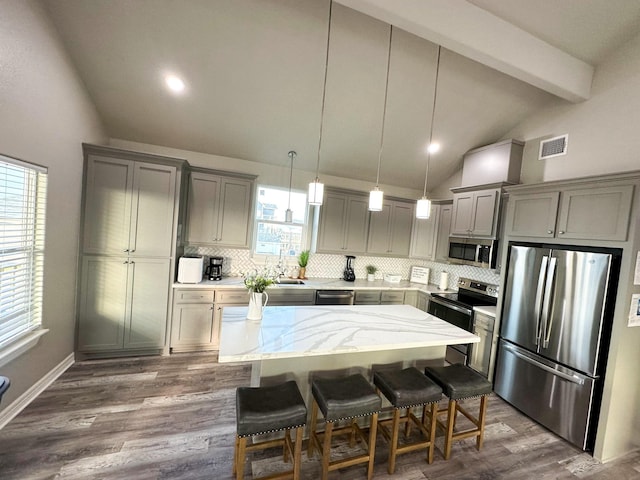 kitchen with a breakfast bar area, decorative light fixtures, lofted ceiling with beams, a kitchen island, and stainless steel appliances