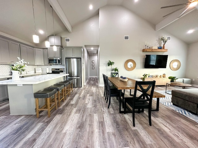 kitchen with gray cabinetry, wood-type flooring, decorative light fixtures, appliances with stainless steel finishes, and a kitchen breakfast bar