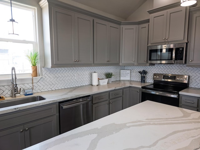 kitchen featuring sink, gray cabinetry, hanging light fixtures, light stone counters, and stainless steel appliances