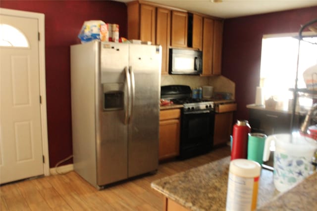 kitchen with light stone countertops, stainless steel fridge, range with gas cooktop, and light hardwood / wood-style flooring