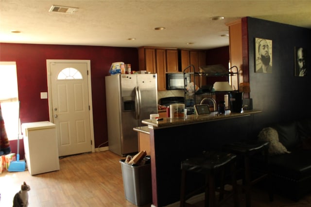 kitchen with a kitchen bar, refrigerator, stainless steel fridge with ice dispenser, light hardwood / wood-style flooring, and kitchen peninsula