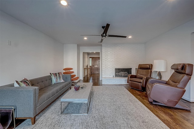 living room featuring a brick fireplace, dark wood-type flooring, and ceiling fan