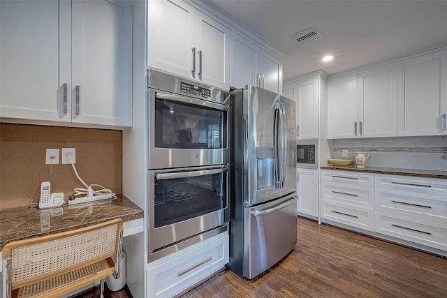 kitchen with white cabinets, dark stone counters, decorative backsplash, stainless steel appliances, and dark wood-type flooring