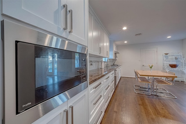 kitchen with sink, wood-type flooring, black microwave, white cabinets, and backsplash