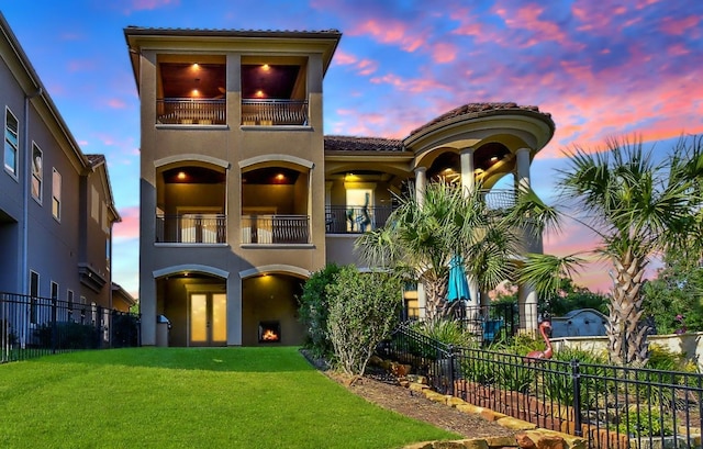 mediterranean / spanish-style house with a lawn, fence, and a balcony