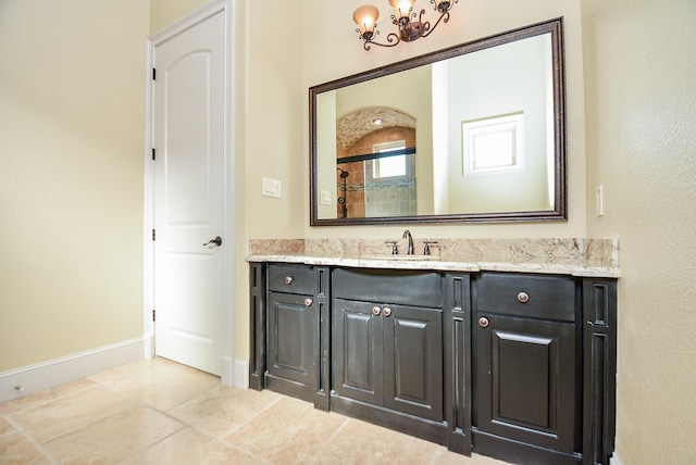 bathroom with vanity, a chandelier, tile patterned flooring, tiled shower, and baseboards