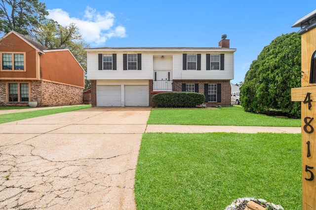 split foyer home with a front yard, driveway, an attached garage, a chimney, and brick siding