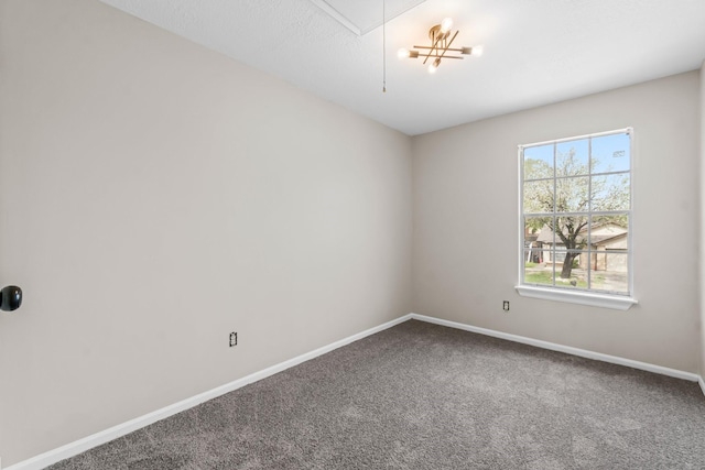 carpeted empty room featuring attic access and baseboards