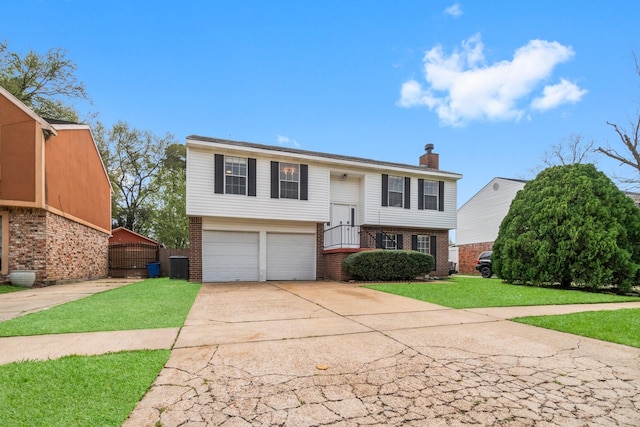 bi-level home featuring driveway, a chimney, brick siding, a garage, and a front yard
