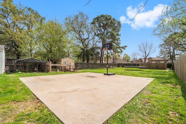 view of sport court featuring a fenced backyard, a yard, and a trampoline