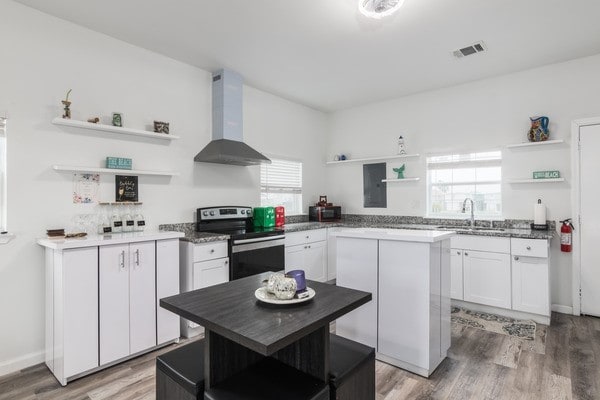 kitchen featuring wall chimney exhaust hood, white cabinetry, stainless steel electric range oven, a center island, and hardwood / wood-style floors