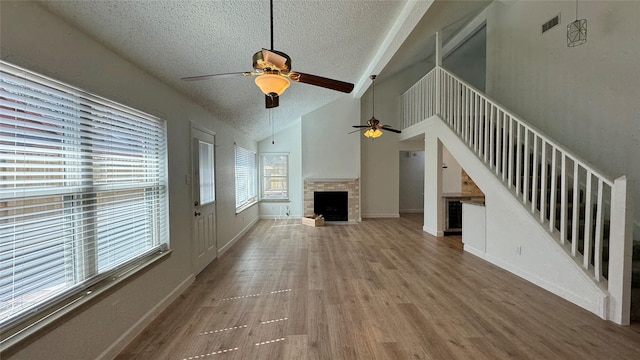 unfurnished living room with visible vents, stairway, wood finished floors, a textured ceiling, and a fireplace