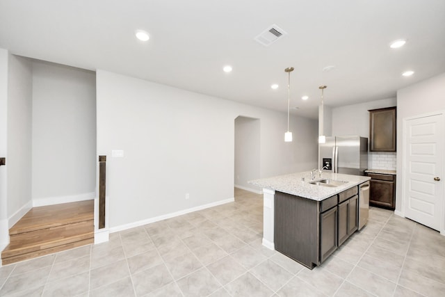 kitchen with appliances with stainless steel finishes, pendant lighting, tasteful backsplash, an island with sink, and dark brown cabinetry