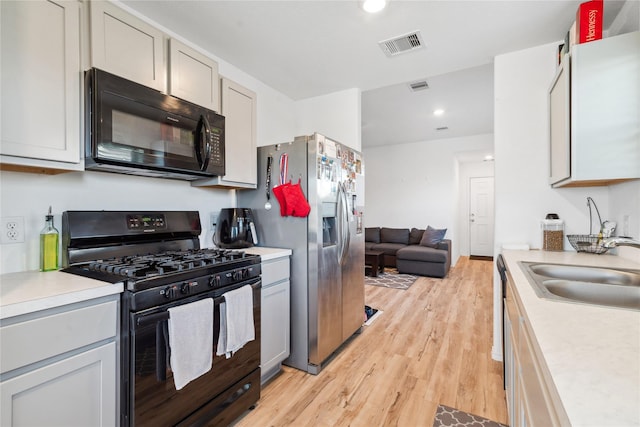 kitchen featuring light wood finished floors, visible vents, light countertops, black appliances, and a sink