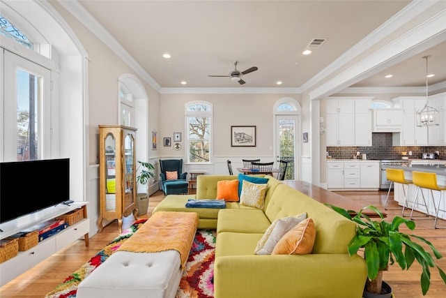 living room featuring crown molding, light hardwood / wood-style flooring, and ceiling fan with notable chandelier