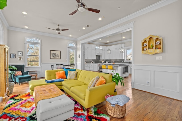 living room with light hardwood / wood-style flooring, a wealth of natural light, ornamental molding, and ceiling fan