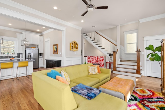 living room featuring ceiling fan, ornamental molding, and light wood-type flooring