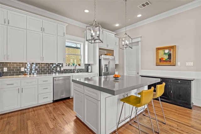 kitchen with light hardwood / wood-style flooring, appliances with stainless steel finishes, white cabinetry, hanging light fixtures, and a center island